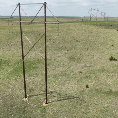 Aerial shot of transmission lines stretching across an open field with Midwest Energy's blue and green logo in the corner.